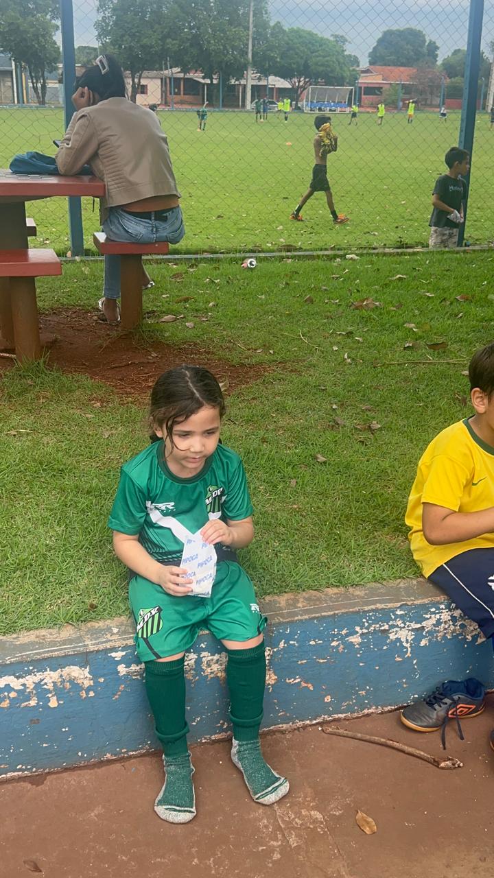 Criança com uniforme do MDV aproveita um lanche ao lado do campo