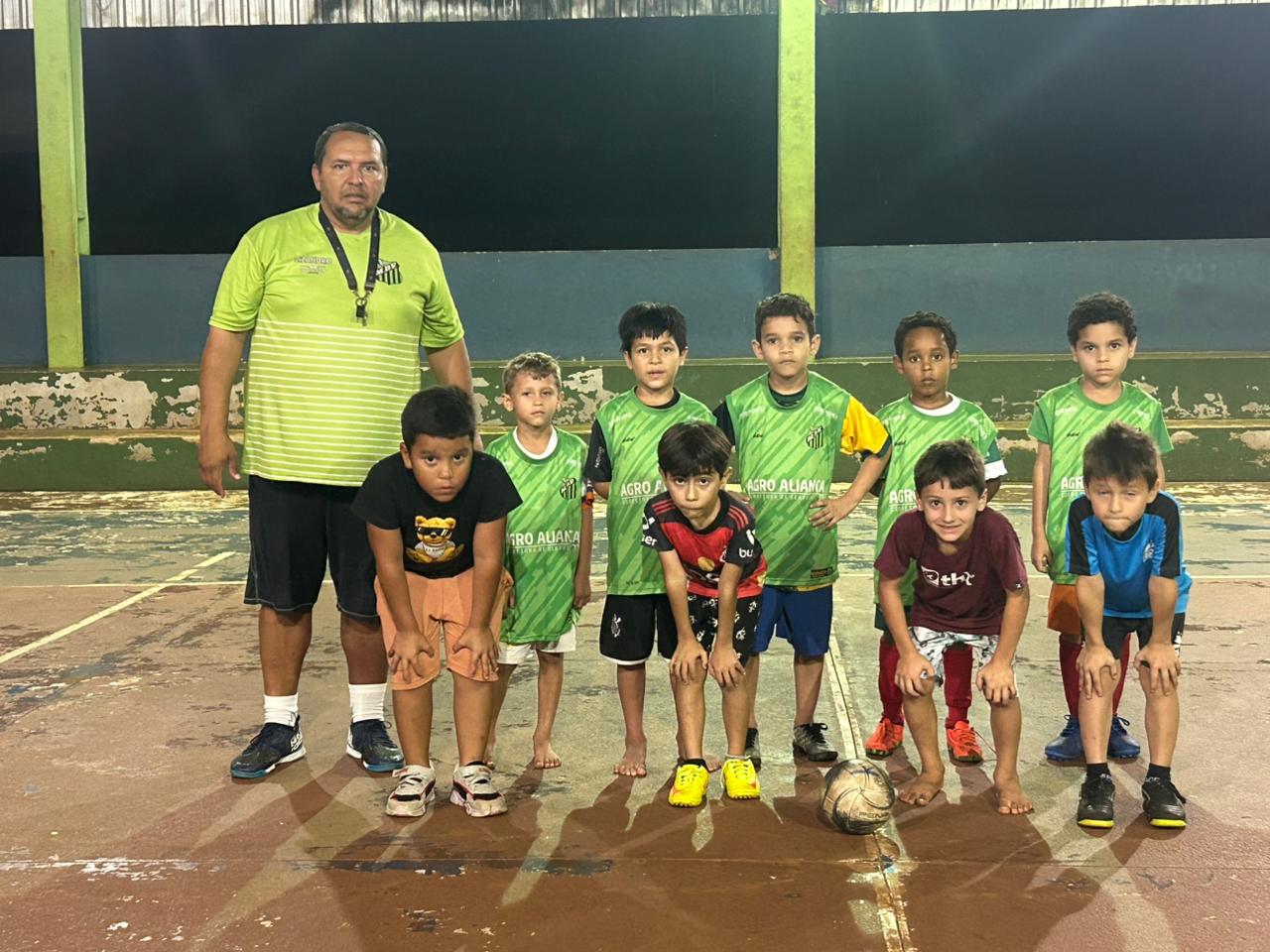 Equipe de atletas mirins posada ao lado do professor na quadra da escola